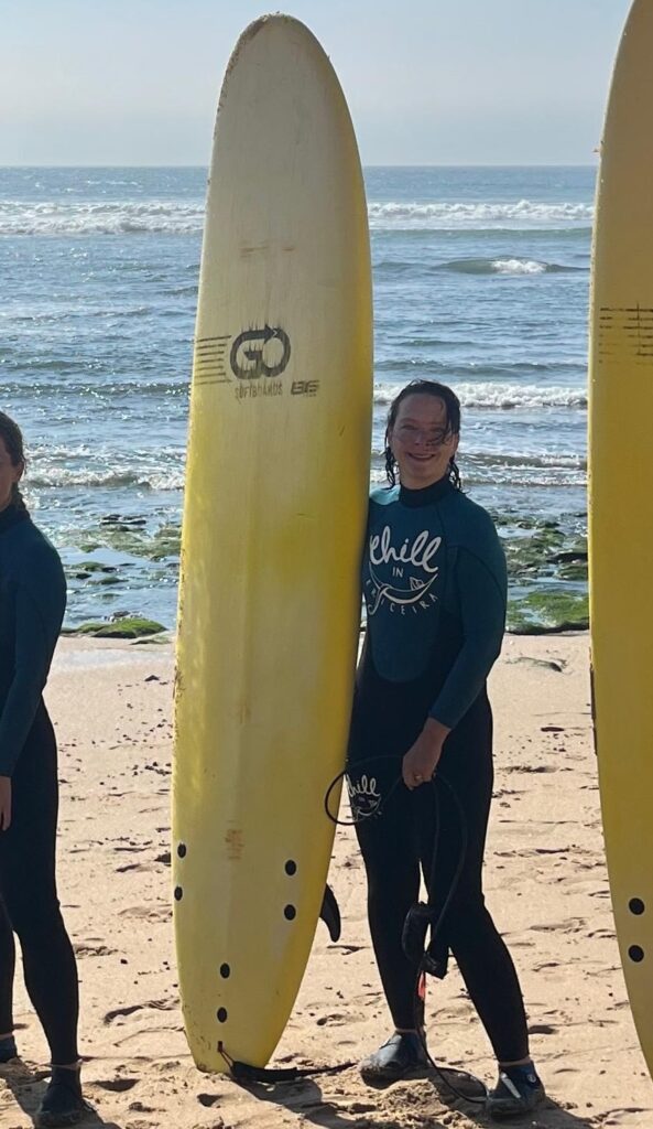 Silke Schütte mit Surfboard am Strand, glücklich